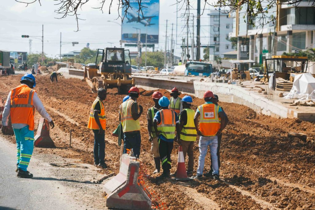 Des ouvriers du bâtiment portant des équipements de sécurité sur un chantier routier animé, en journée.